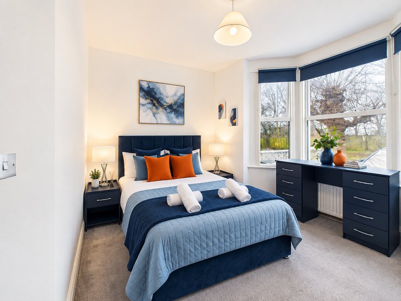 Modern bedroom with navy bed, orange pillows, wooden dresser, pendant light and bay window