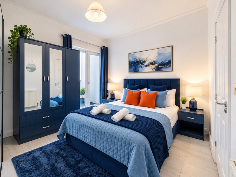 Modern bedroom with navy bed frame, orange pillows, wardrobe and bedside lamps
