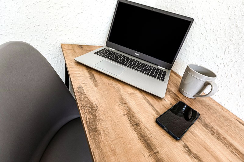 Wooden desk with laptop, coffee mug, phone, and office chair