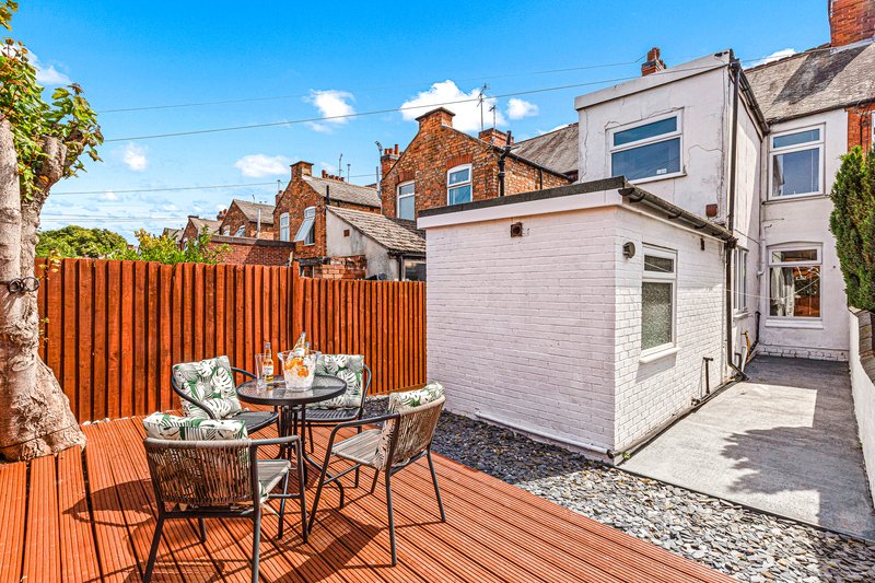 Rear garden with wooden deck, outdoor seating, and brick terraced houses