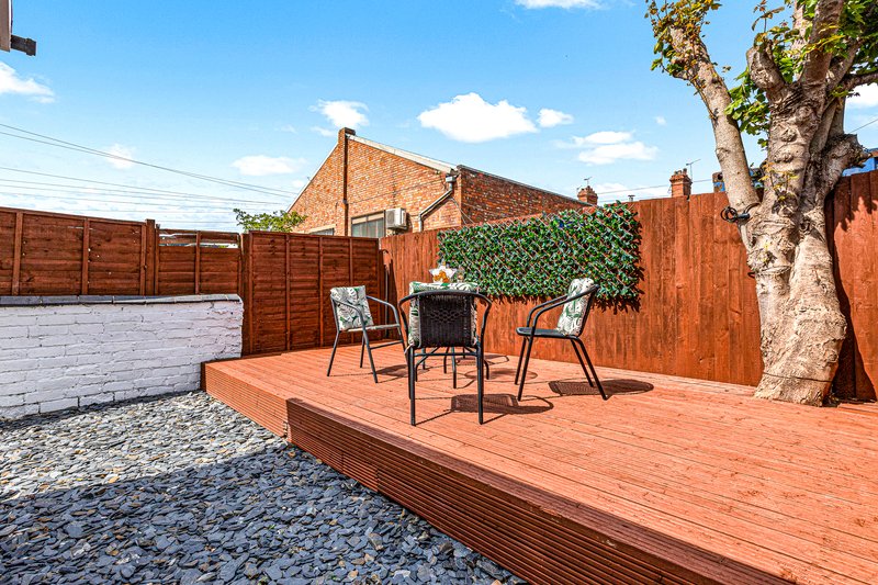 Brick property with wooden deck, seating area, tree, and brown fencing