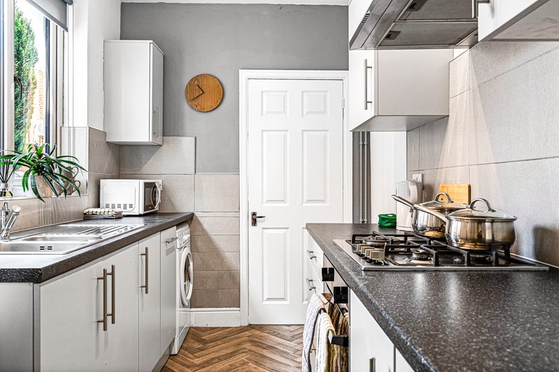 Modern kitchen with white cabinetry, black countertops, gas hob, and wooden flooring