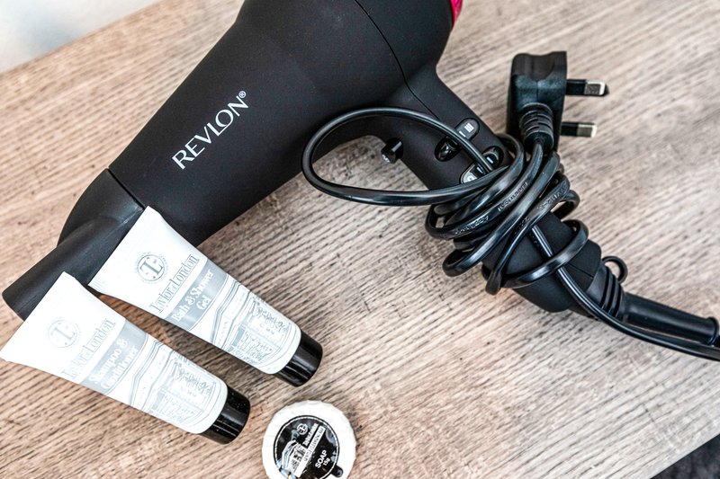 Hair dryer, styling tools, and toiletries arranged on wooden surface