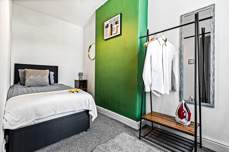 Bedroom with single bed, green accent wall, clothing rack, and grey carpet flooring