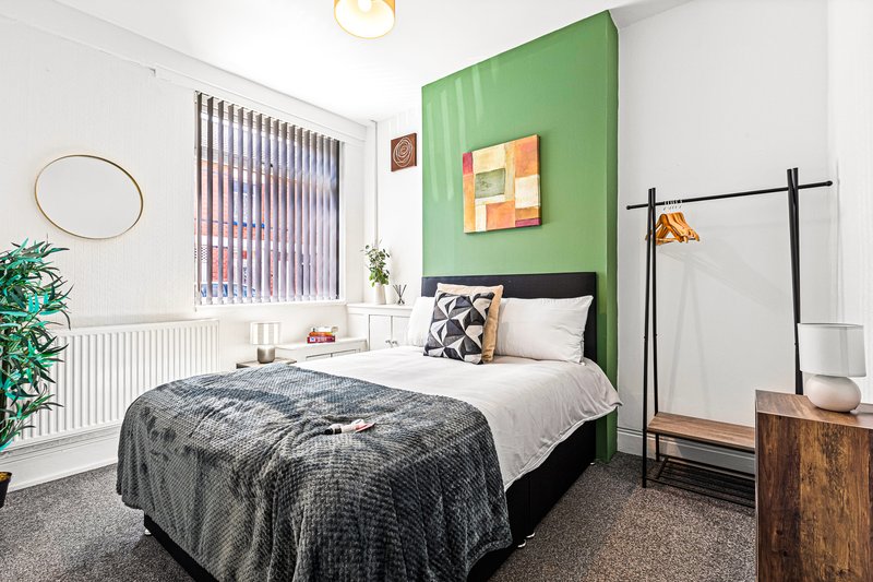 Modern bedroom with double bed, green accent wall, geometric artwork and contemporary furnishings