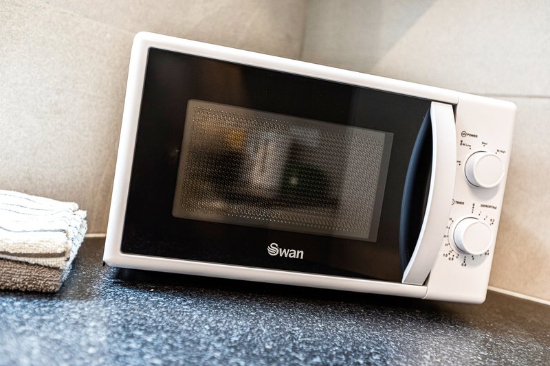 White microwave oven on kitchen counter with control dials and folded towels nearby