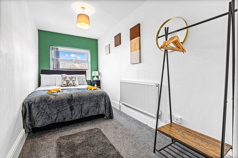 Compact bedroom with single bed, green headboard, wooden clothes rail and ceiling lamp