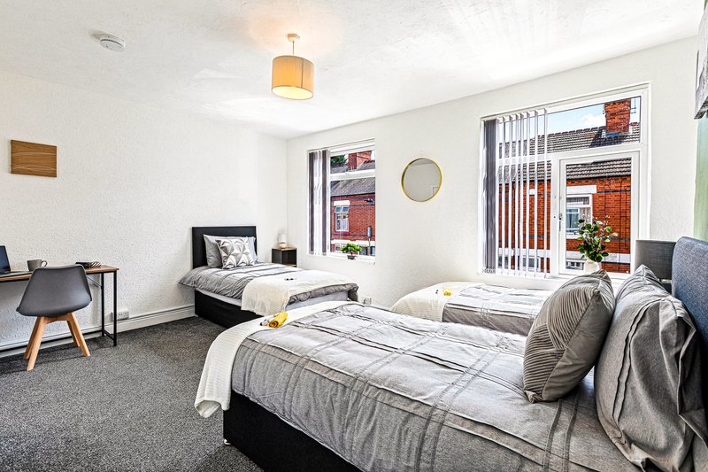 Bright twin bedroom with two single beds, desk, chair, and window with vertical blinds