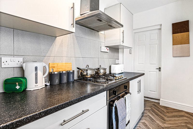 Modern kitchen with white cabinetry, dark granite countertop, stainless steel range hood and appliances