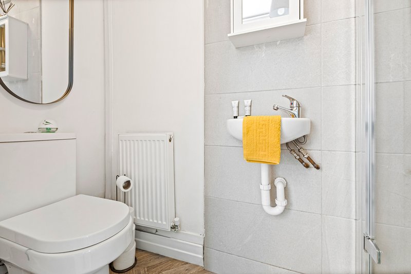 Clean bathroom with white toilet, wall-mounted sink, yellow towel and round mirror