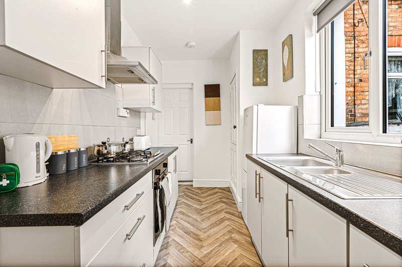 Modern kitchen with white cabinetry, dark countertops, gas hob and herringbone wood flooring
