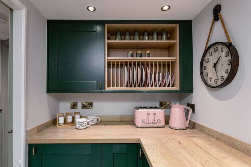 Kitchen corner with green cabinetry, wooden countertop, open dish rack, and pink appliances