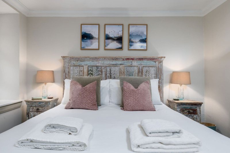 Bright bedroom with double bed, decorative headboard, bedside lamps and framed wall art