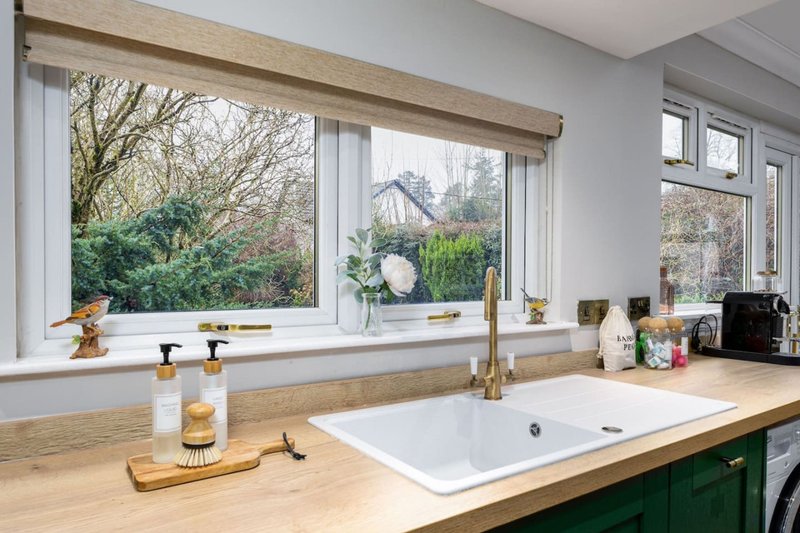 Modern kitchen with wooden countertop, white sink, brass faucet and large windows overlooking garden