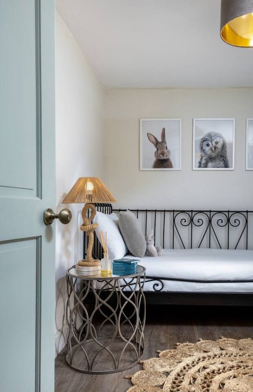 Bedroom with black metal daybed, gold table lamp, framed animal prints, and woven rug