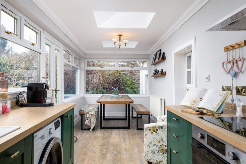 Bright kitchen with green cabinetry, wooden countertops, and garden views through large windows