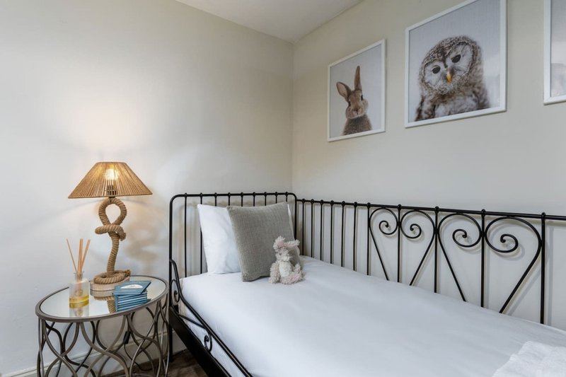 Bedroom with single metal bed, white bedding, side table lamp, and framed animal wall art