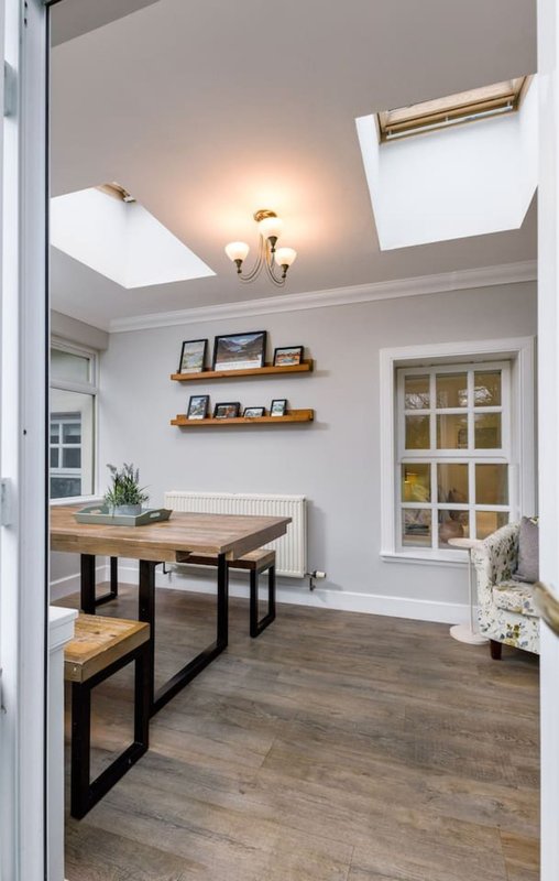 Bright dining nook with wooden table, bench seating, floating shelves and skylights