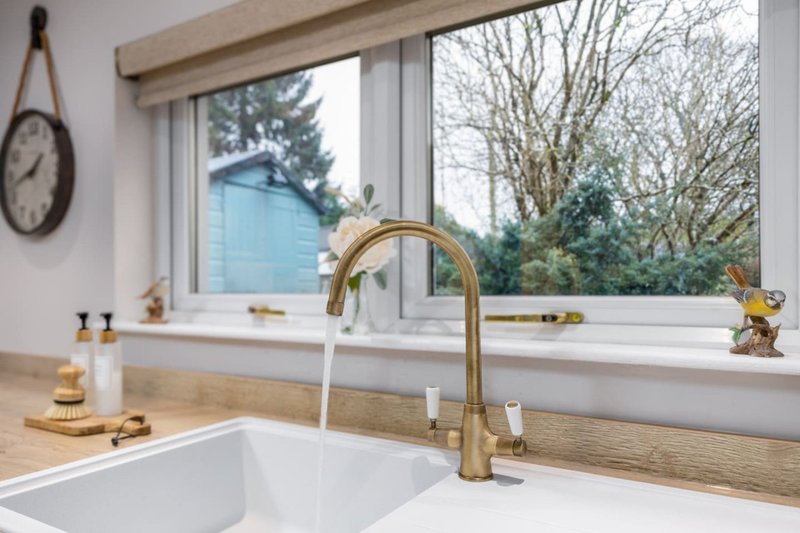 Modern kitchen sink with brass faucet, wooden countertop, window overlooking garden