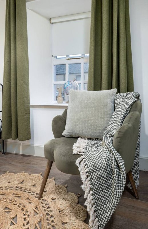 Cozy reading nook with green armchair, cushions, throw blanket and window view