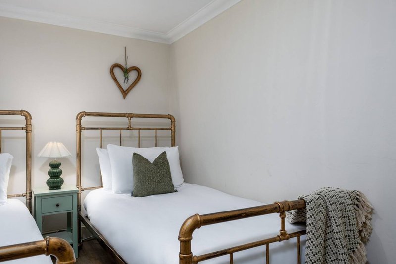 Bright bedroom with two single beds, brass frames, white bedding, green cushion, and wooden heart decoration
