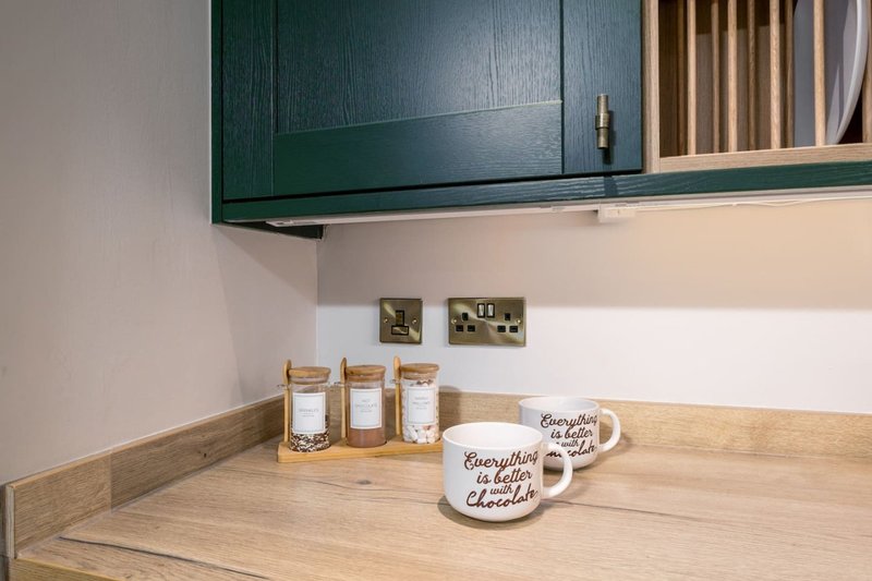 Kitchen counter with green cabinetry, wooden countertop, storage jars, and decorative mugs