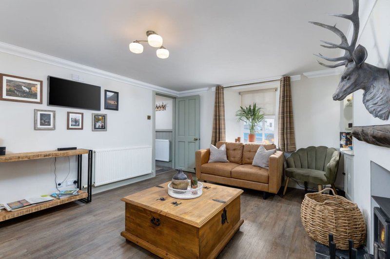 Open-plan living room with tan sofa, wooden coffee table, fireplace and decorative deer head