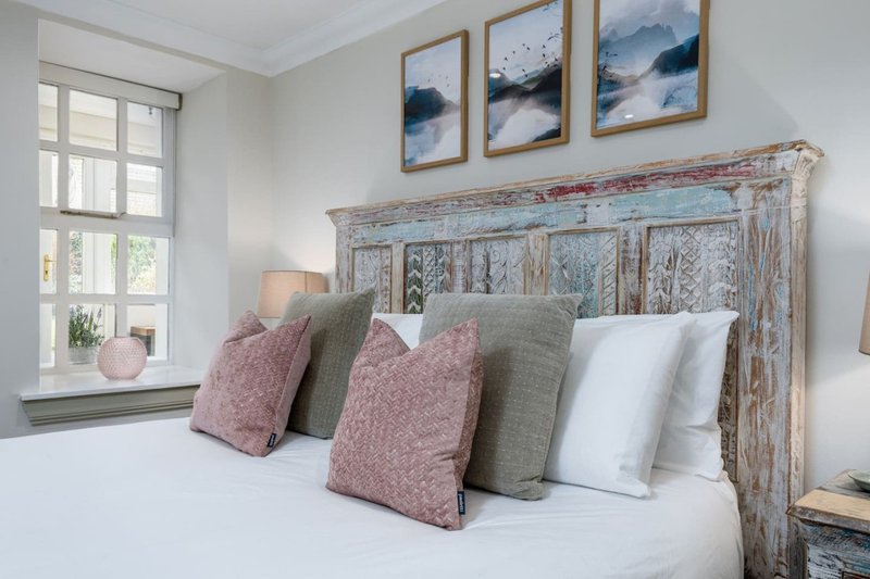 Bright bedroom with distressed blue headboard, decorative pillows, mountain artwork and window seat