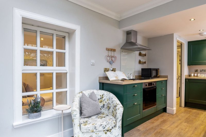 Modern kitchen with green cabinetry, dark range hood, and patterned armchair by window