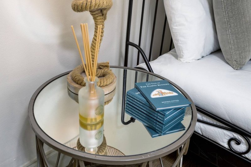 Bedside table with reed diffuser, blue books, and lamp near bed