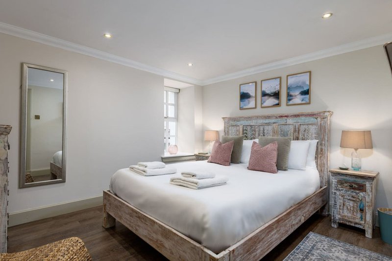 Bright bedroom with large bed, wooden headboard, pink cushions, bedside lamp and framed artwork