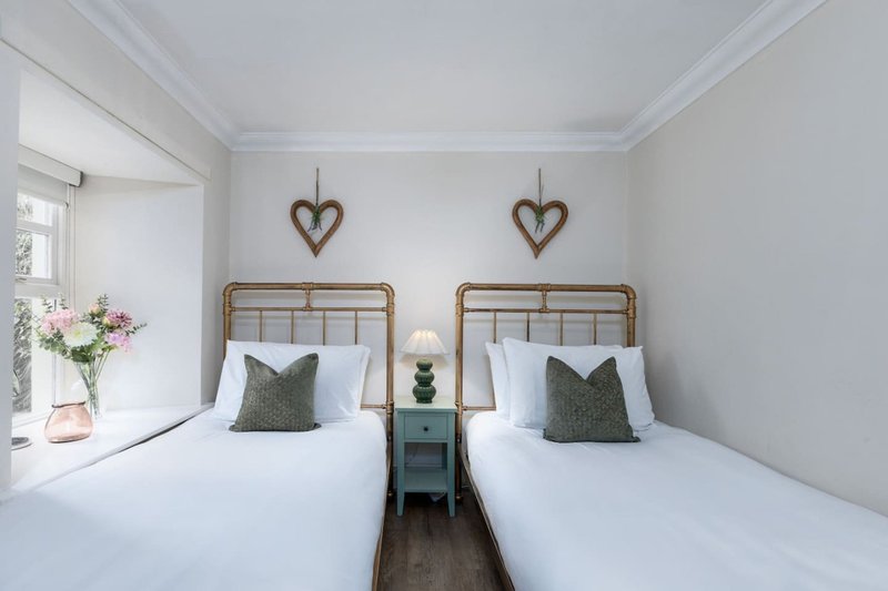 Bright twin bedroom with two single beds, wooden frames, white linens, green cushions, heart decorations and window