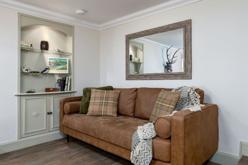 Living room with brown leather sofa, patterned cushions, built-in shelving unit, and framed mirror