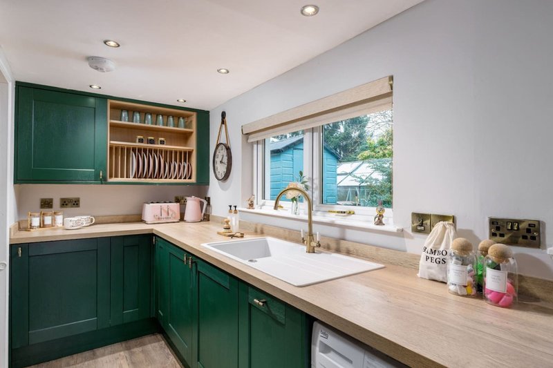 Modern kitchen with green cabinetry, wooden countertop, white sink and window view