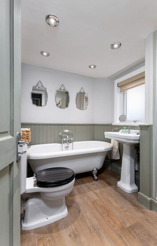 Bathroom with freestanding bathtub, pedestal sink, toilet, and three wall mirrors