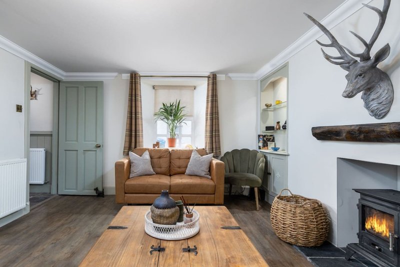 Living room with tan leather sofa, fireplace, deer head mount, and wood flooring