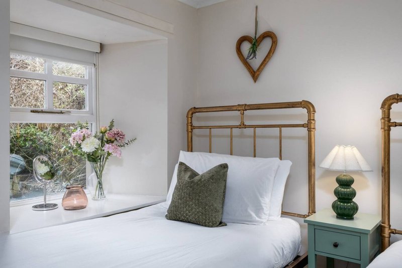 Bright bedroom with rattan bed frame, white bedding, green cushion, wooden heart decoration, and window with flowers