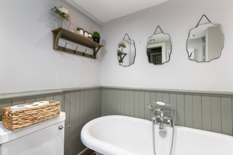 Modern bathroom with freestanding bathtub, grey panelling, three mirrors and floating shelf with decor