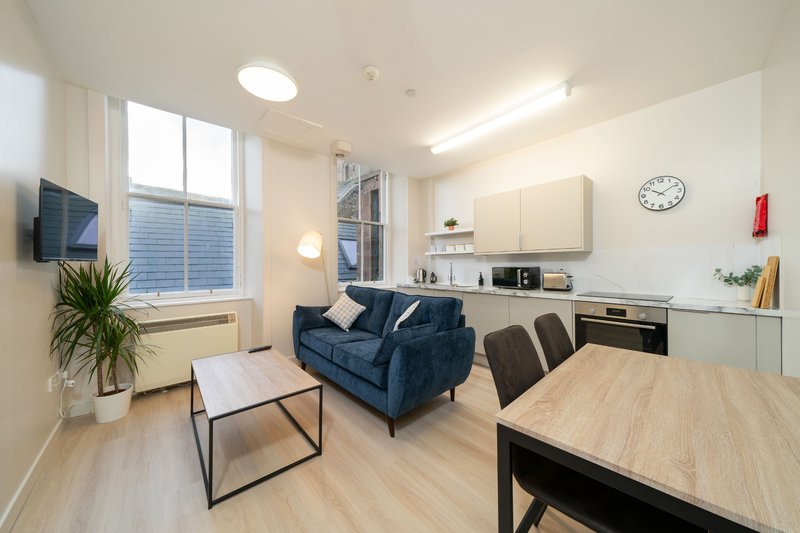 Modern open-plan apartment with blue sofa, dining table, kitchenette and large window