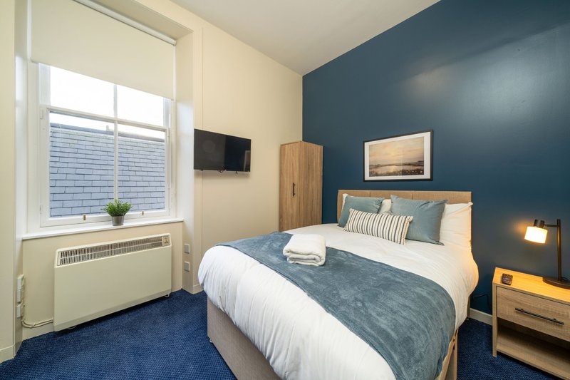 Modern bedroom with double bed, blue accent wall, wooden furniture and window