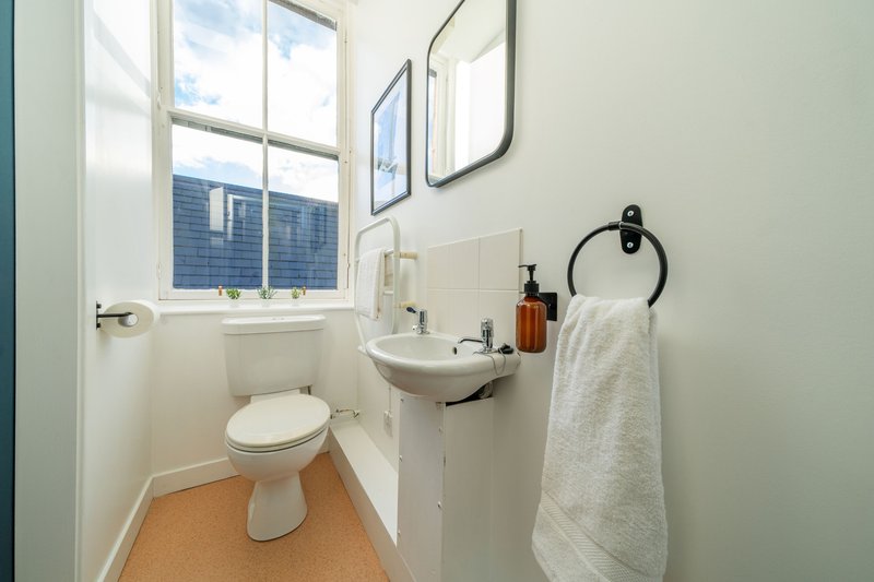 Compact bathroom with toilet, wall-mounted sink, window, and towel rail