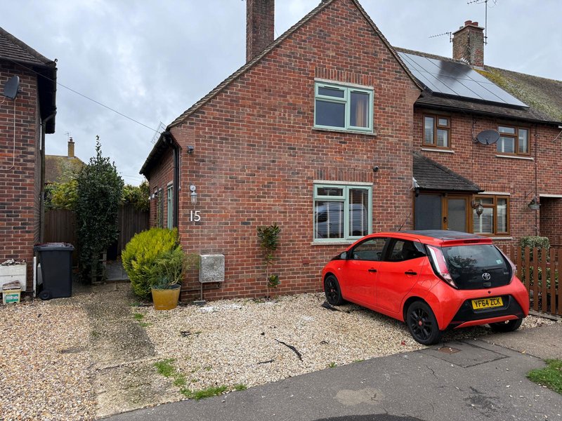 Red brick semi-detached house with driveway, parked red car, and front garden