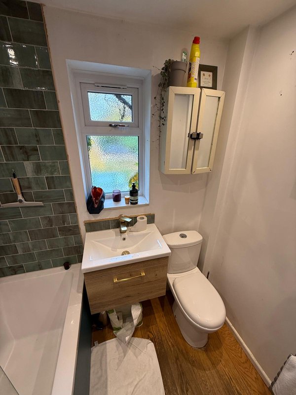 Bathroom with white toilet, wooden vanity sink, green tile shower, and window with frosted panes
