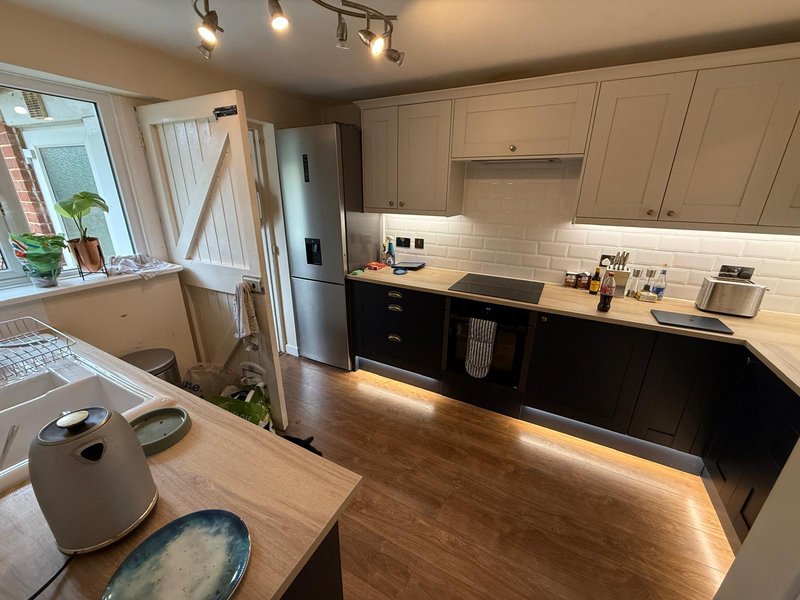 Modern kitchen with cream and black cabinetry, wooden countertops, stainless steel appliances, and dining table
