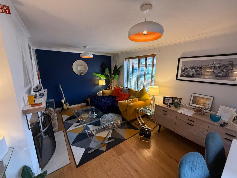 Modern living room with blue accent wall, yellow armchair, geometric rug and pendant lighting