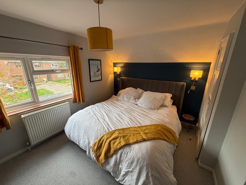 Modern bedroom with double bed, gold bedding, wall-mounted headboard with lights, and garden view