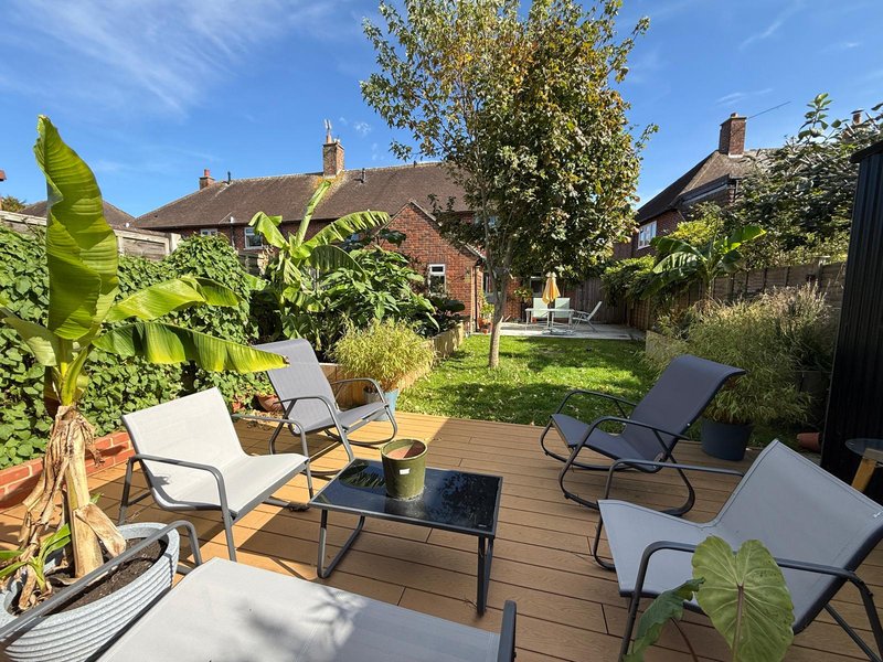 Garden seating area with wooden deck, lounge chairs, potted plants and brick houses