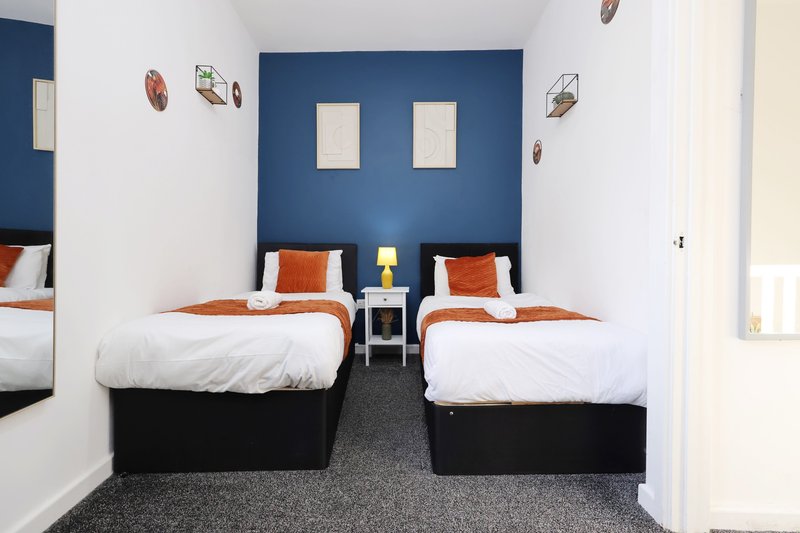 Twin bedroom with dark blue accent wall, orange pillows, white bedding, and shared nightstand