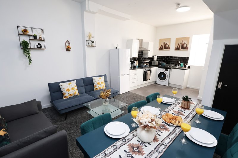 Open-plan living and kitchen area with blue sofa, dining table set for a meal, and modern appliances