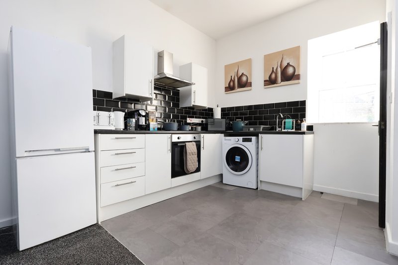 Modern kitchen with white cabinetry, black tile splashback, integrated appliances and gray flooring